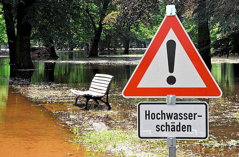 überschwemmter Parkweg neben Hochwasser-Warnschild 